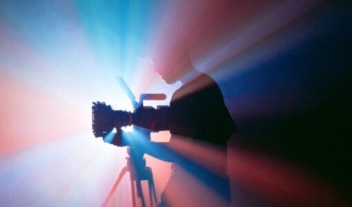 Silhouette einer Person mit Filmkamera auf einem Stativ im farbigen Licht