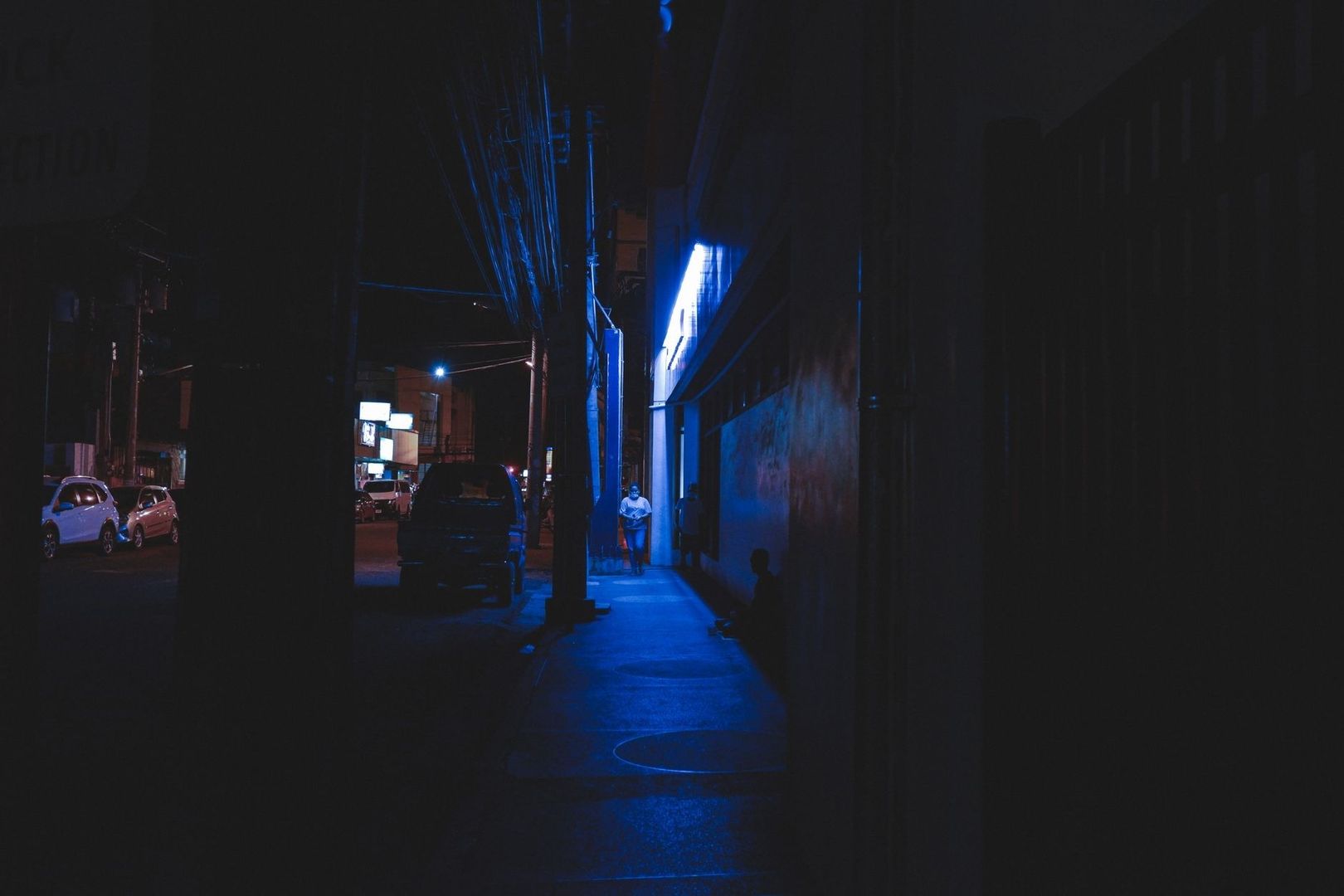 Dunkle nächtliche Gasse mit blauem Neonlicht und geparkten Autos
